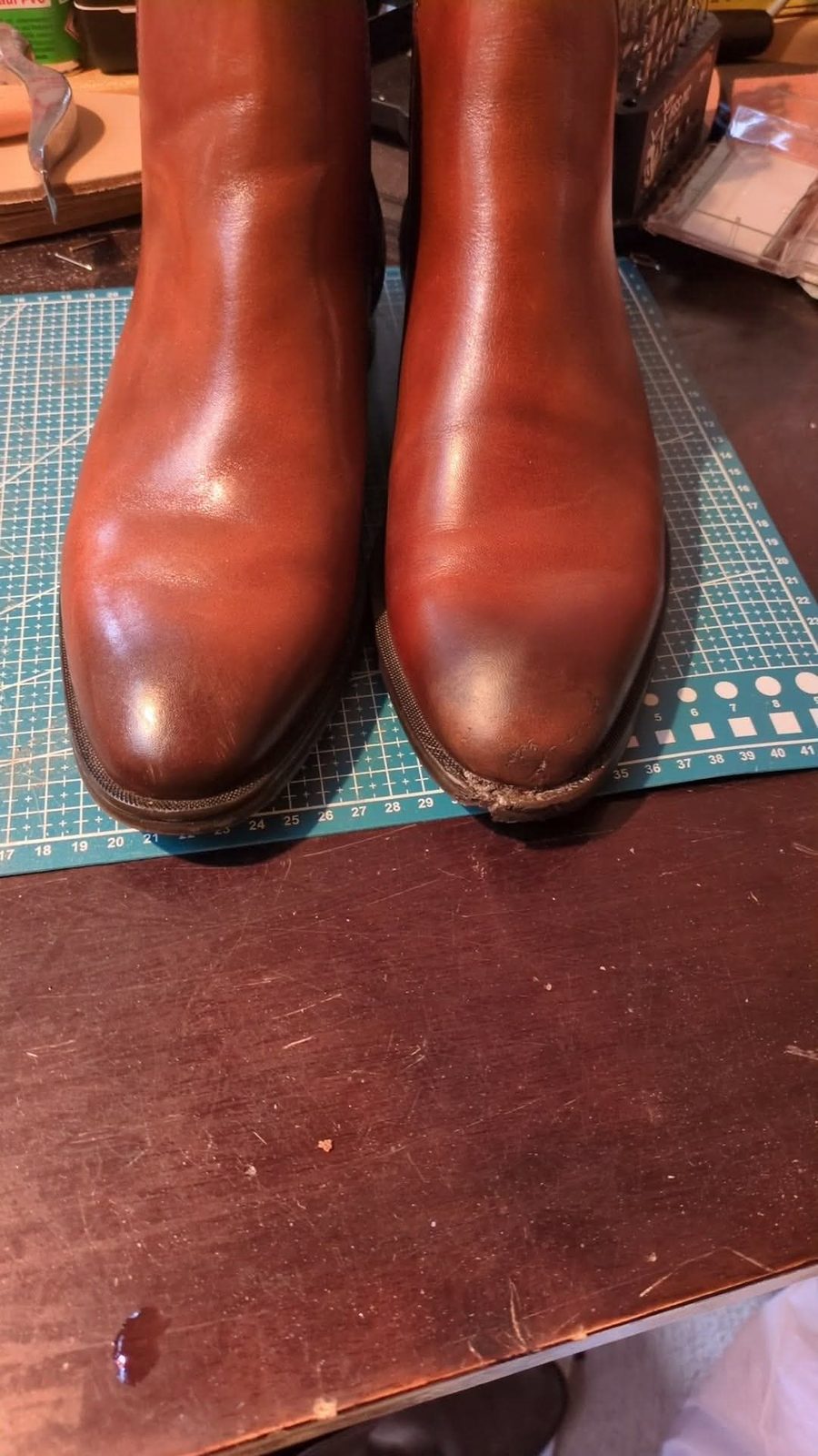 Tan leather Chelsea boots on a cutting mat, sole separating from the upper at the right toe