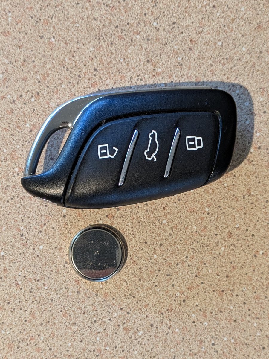 A three-button car key fob beside the CR2032 coin cell removed from it