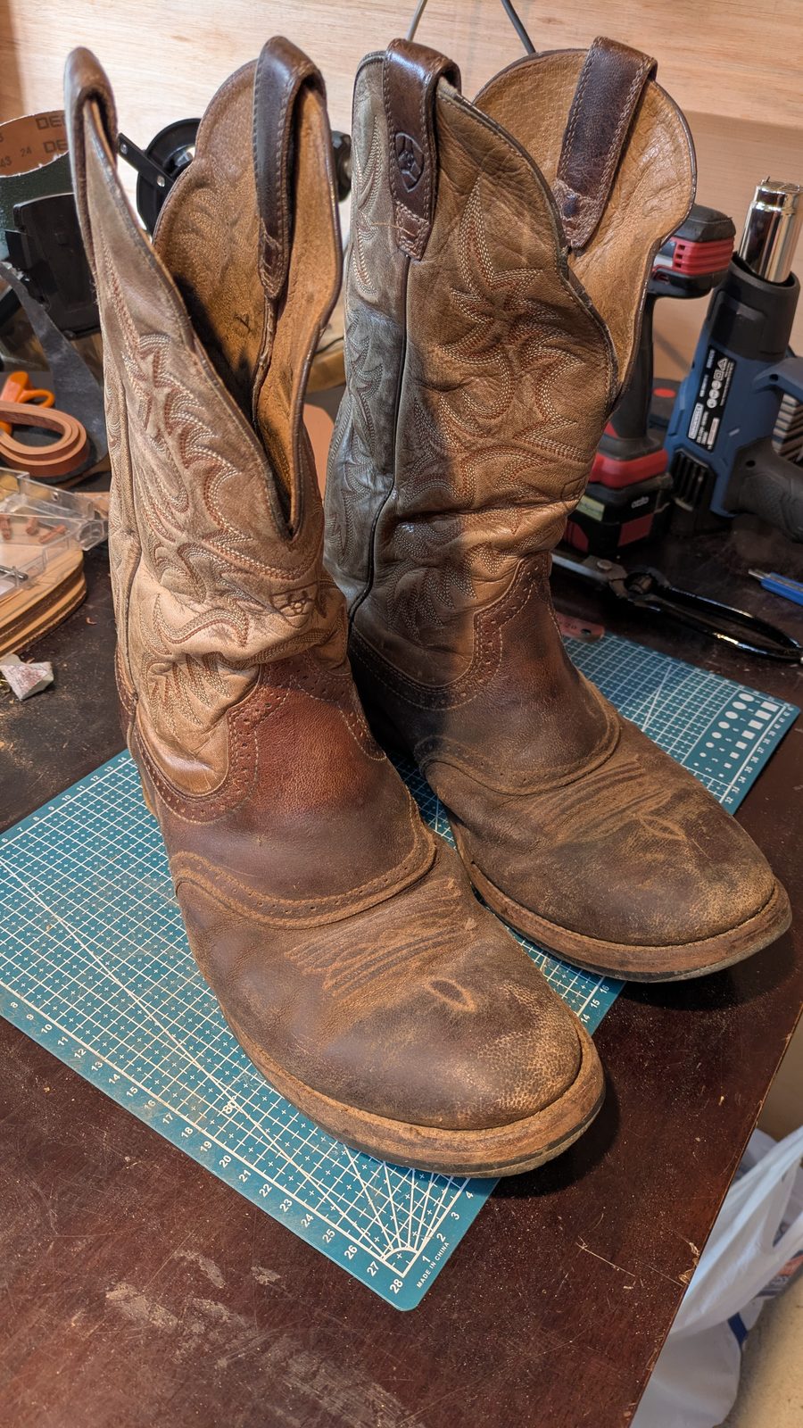 A well-worn pair of tooled western riding boots standing on the workshop bench